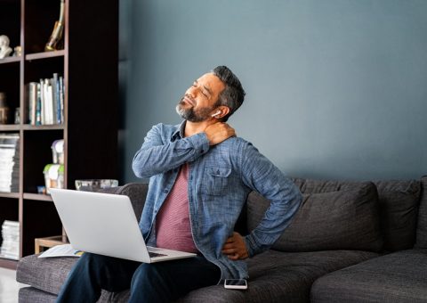 Man sitting on couch with laptop rubbing neck.